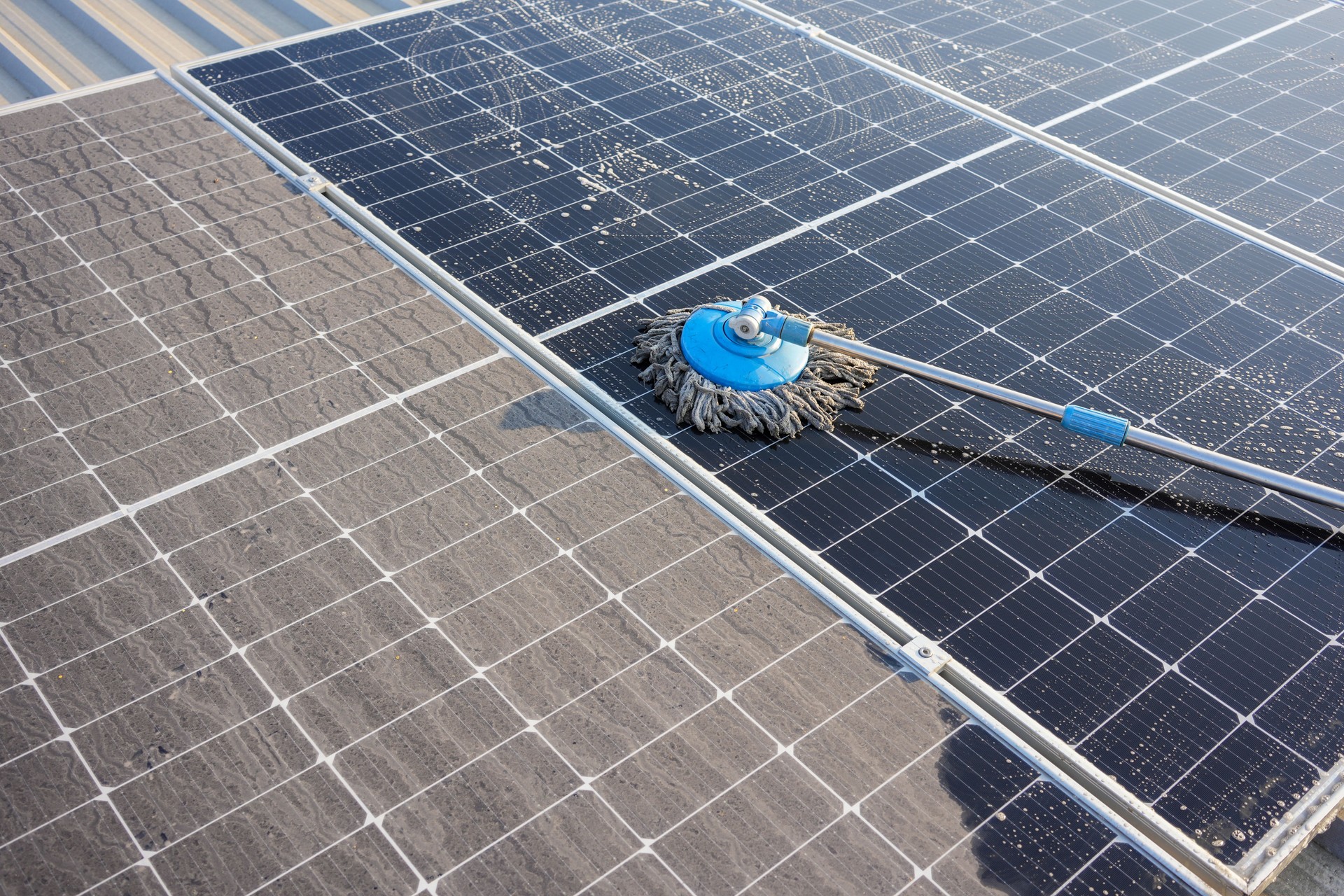 Man using a mop and water to clean the solar panels that are dirty with dust and birds' droppings to improve the efficiency of solar energy storage.